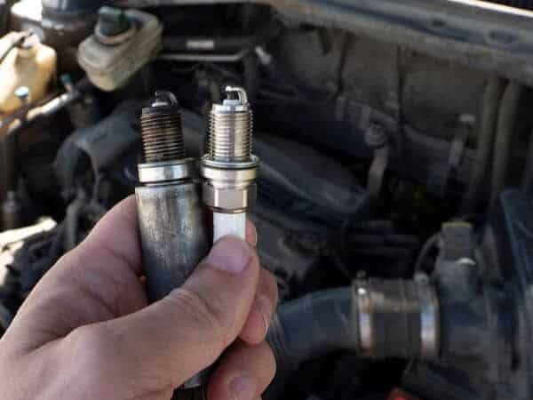 Tune up service at Little Wolf Automotive, image of closeup of mechanic holding up 2 spark plugs in front of car engine