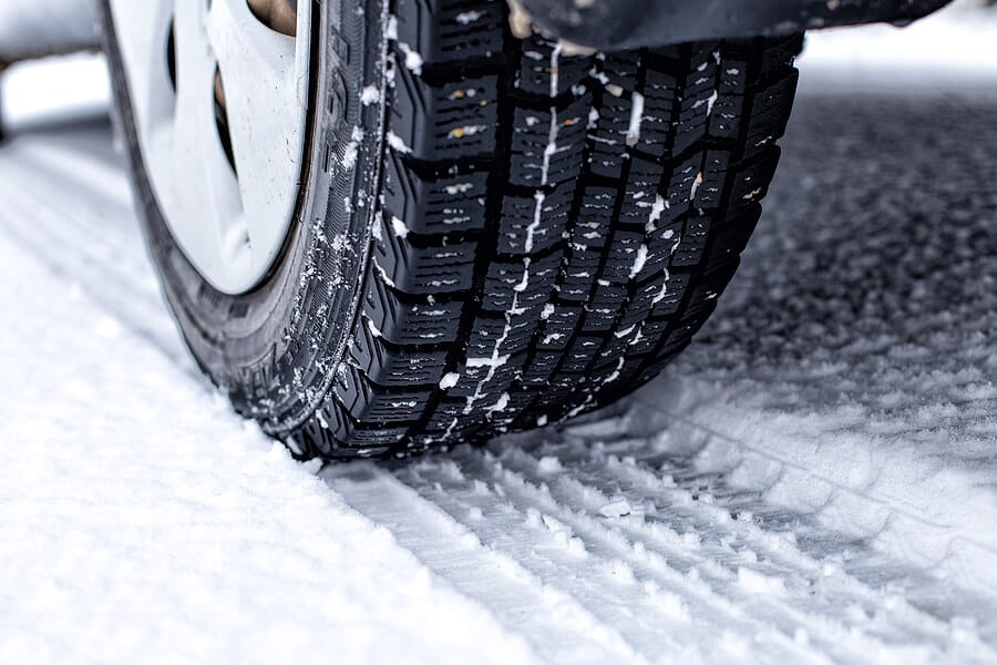 closeup image of snow tire on vehicle with tire track in snow on road