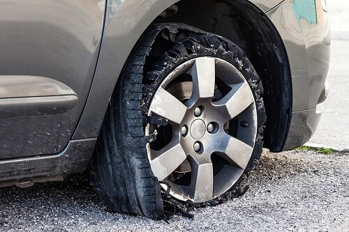 What to Do If You Have a Tire Blowout | Little Wolf Express Lube in Antigo, WI. Image of a blown-out tire with exploded, shredded rubber on a modern SUV automobile.