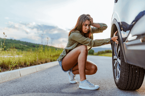 Can You Drive on a Slow Leaking Tire? | Little Wolf Automotive at Antigo, WI. Image of a young worried woman checking her car tires on the road.
