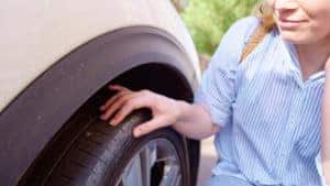 When to Repair or Replace Tires | Little Wolf Automotive in Antigo, WI. Image of a woman inspecting the puncture site on the flat tire of her car.