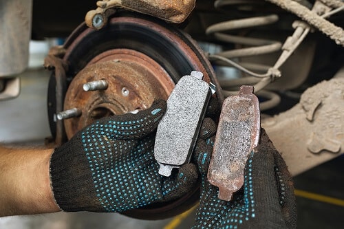 What Happens If I Don't Change Brakes For a Long Time? | Little Wolf Automotive in Waupaca, WI. Closeup image of a car mechanic comparison a worn brake and a new one. In the background is a corroded brake disc.