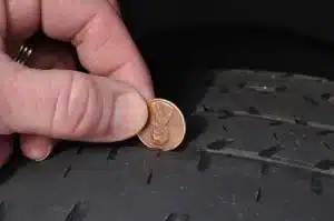 5 Signs You Need New Tires | Little Wolf Automotive in Antigo, WI. Closeup image of a mechanic’s hand inspecting tread of a worn tire using a penny.