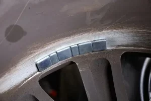 What Maintenance Do My Tires Need? | Little Wolf Automotive in Plover, WI. Image of balancing lead mounted on car wheel to correct imbalances of tire. Tire alignment is a tire maintenance task.