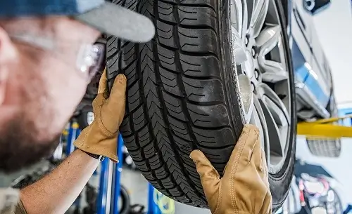 How Do I Get My Tires Ready for Winter? | Little Wolf Automotive in Antigo, WI. Closeup image of a mechanic replacing summer tires with winter tires. Tire tread is also shown.