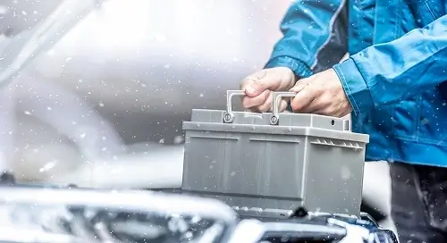 Keep Your Car Battery from Dying in Cold Weather | Little Wolf Automotove in Waupaca, WI. Image of a car technician replacing a dead car battery in winter conditions.