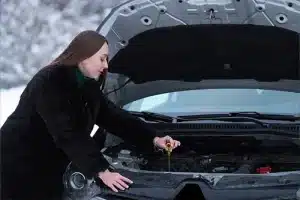 5 Simple Tips for Changing Oil This Winter | Little Wolf Automotive in Plover, WI. Image of a woman checking the oil in the engine of her car in winter. Concept image of preparing the car for winter driving.