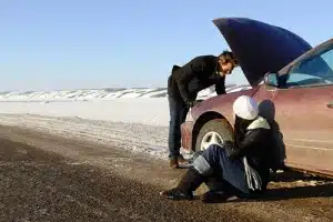 Pre-Trip Vehicle Inspection: A Few Things to Check Before Your Holiday Trip | Little Wolf Automotive in Waupaca, WI. Image of a couple stranded at side of highway with a car breakdown in winter.