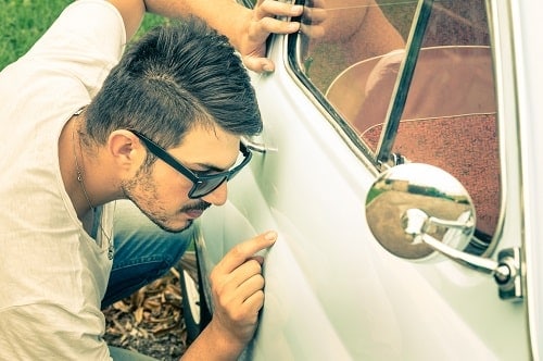 Small Changes, Big Returns: 5 Simple Ways to Boost Your Car's Resale Value | Little Wolf Auto in Waupaca, WI. Image of a man checking any dent or scratches on a white car that's on resale.