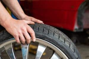 An auto mechanic holding and changing a car tire according to the season. Concept image of “Don't Hit the Road Without These 8 Spring Car Care Tips” | Little Wolf Auto in Plover, WI.