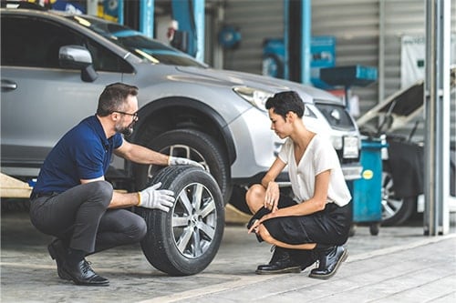 A male mechanic man showing the tread of a old tire to a female customer at an auto repair center. Concept image of “5 Tips to Keep Your Tires Safe and Optimal ” | Little Wolf Auto in Plover, WI.