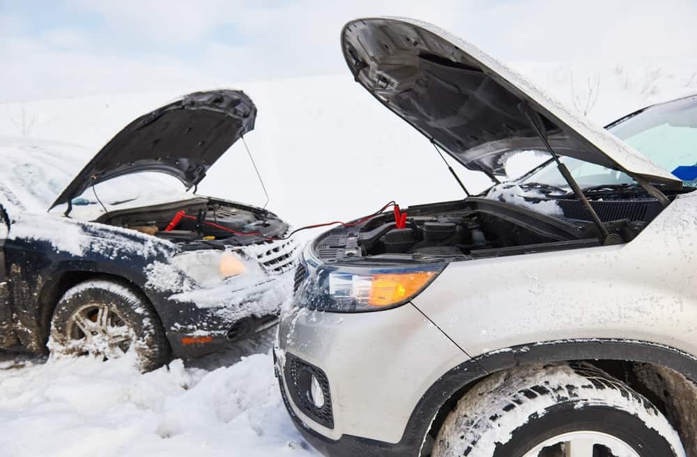 Protect Your Car Battery in Cold Weather | Little Wolf Auto Repair. Image of two cars with jumper cables hooked up to their batteries in the snow.