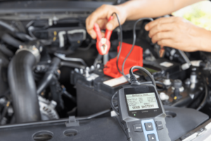 Don’t Get Stranded: Why Fall is the Perfect Time for Car Battery Service. Mechanic using a battery tester on a car engine.