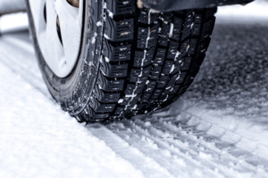 winter tires, auto repair in Antigo, WI at Little Wolf Express Lube. Close-up of a car tire with winter treads driving on a snow-covered road.