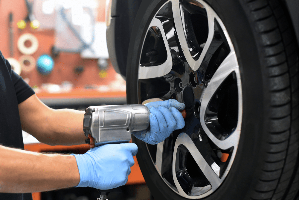 front-wheel drive tire rotation, auto repair in Little Wolf Automotive at Antigo, WI. Image of a mechanic using a power tool to tighten wheel bolts.