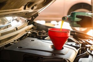 Oil Change in Antigo, WI by Little Wolf Automotive. Image of a mechanic pouring synthetic oil into an engine funnel during summer service.