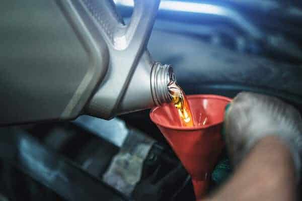 Scheduled maintenance and factory recommended maintenance in Waupaca, WI, image of mechanic with gloves pouring oil into red funnel for engine