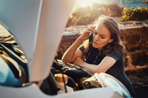 What to do when your car won't start with Little Wolf Automotive, Waupaca WI, Young attractive woman is bent down talking on the phone with the hood up on her car that won't start