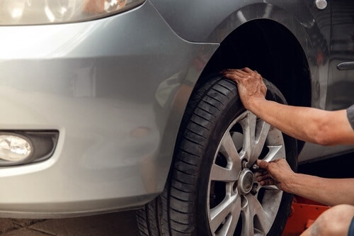 Tire Maintenance and Replacement In Waupaca, WI Little Wolf Automotive image of mechanic checking driver side tire on silver sedan