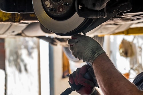 The Importance of Brake Maintenance in Waupaca Wi with Little Wolf Automotive image up lifted car in shop bay, mechanic using tool on exposed brake system