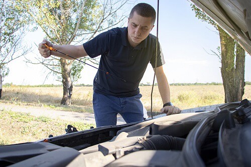 How Often Should I Check My Vehicle's Oil? | Little Wolf Express Lube in Plover, WI. Image of a man holding a dipstick to measure the level of car engine oil.