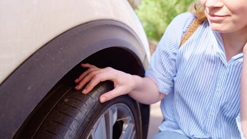 When to Repair or Replace Tires | Little Wolf Automotive in Antigo, WI. Image of a woman inspecting the puncture site on the flat tire of her car.