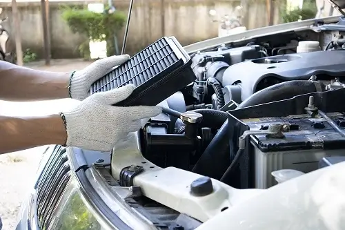 Does Vehicle Maintenance Affect Your MPG? Little Wolf Automotive in Antigo, WI. Image of a car mechanic changing the clogged air filter to maintain engine performance.