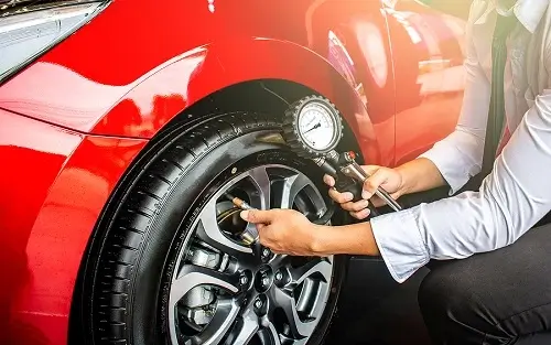 Does Vehicle Maintenance Affect Your MPG? Little Wolf Automotive in Antigo, WI. Image of a man using a gauge to check tire pressure of a red car.