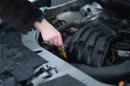 Do I Need to Change Oil Before the Cold Months? | Little Wolf Automotive in Antigo, WI. Image of a woman checking the oil level of her car in preparing for winter conditions. Concept image of oil change.