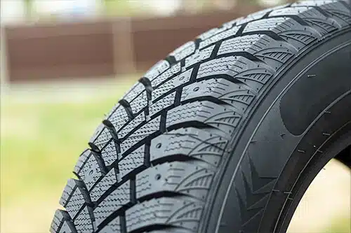 Should You Change Your Tires This Fall? | Little Wolf Automotive in Plover, WI. Closeup image of a car’s tire tread with blurred image of a yard in the background.