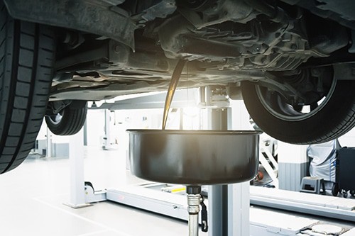 Auto is on hydraulic lift in garage workshop, process of draining old dark used oil preparing for oil change | Little Wolf Automotive in Antigo, WI