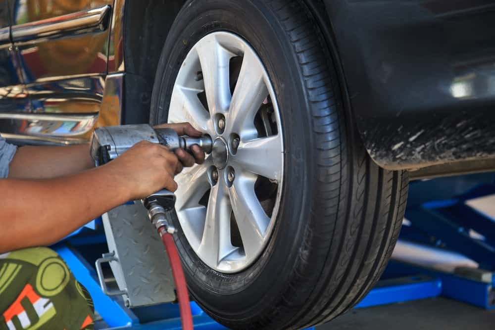 Tire installation near me in Antigo, WI with Little Wolf Express Lube. Image of mechanic using air tool to take old tire off of car that came in for new tires to be installed.