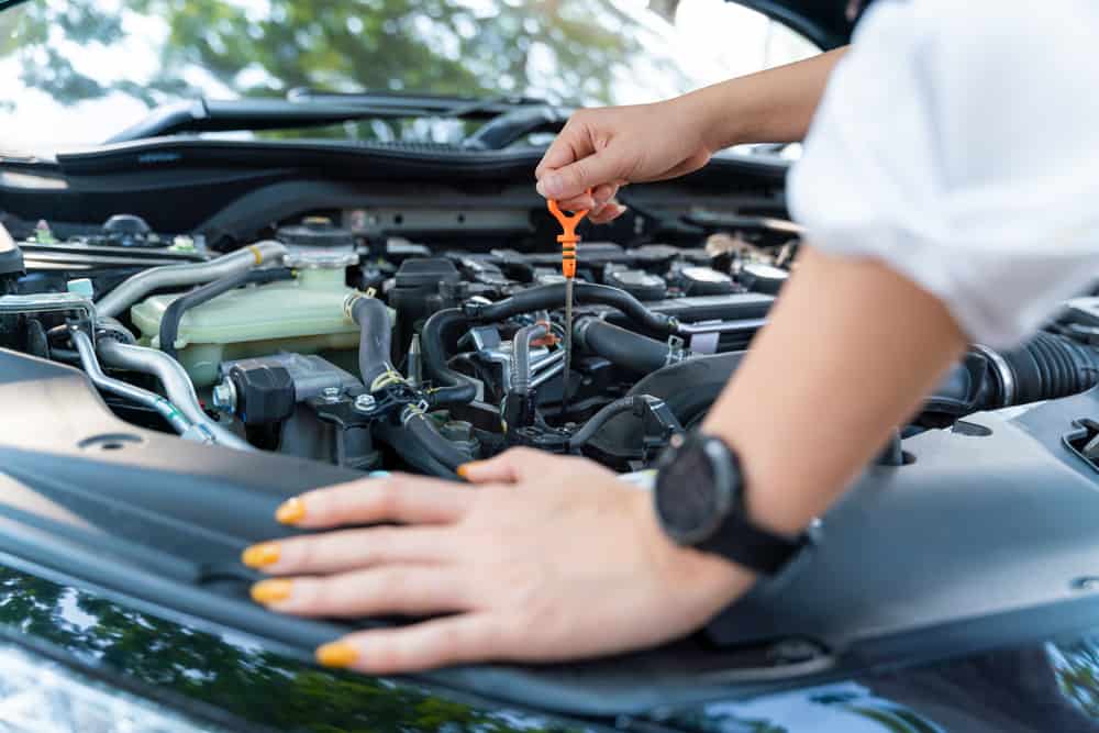 Car maintenance in Waupaca, WI at Little Wolf Express Lube. Image of hand of woman under car hood checking the oil level in car engine for spring car care maintenance