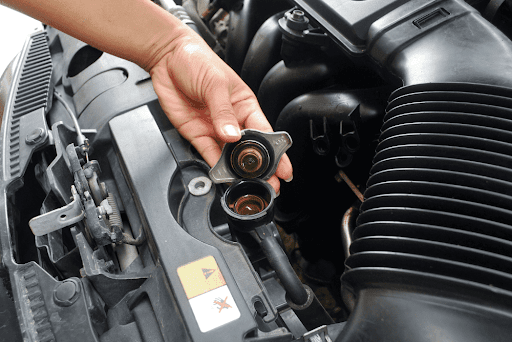 Cooling system check and seasonal maintenance in Antigo, WI with Little Wolf Express. Image of mechanic hand holding the cooling system radiator cap on car engine.
